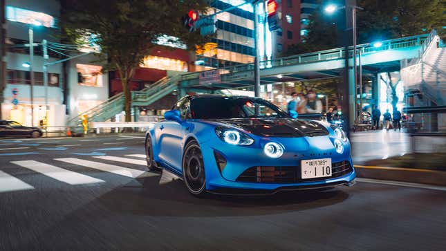 Front-quarter view of a blue Alpine A110 R turning onto a street in a Japanese city
