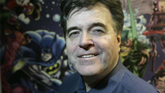Neal Adams smiles at the camera with a mural of DC superheroes behind him.