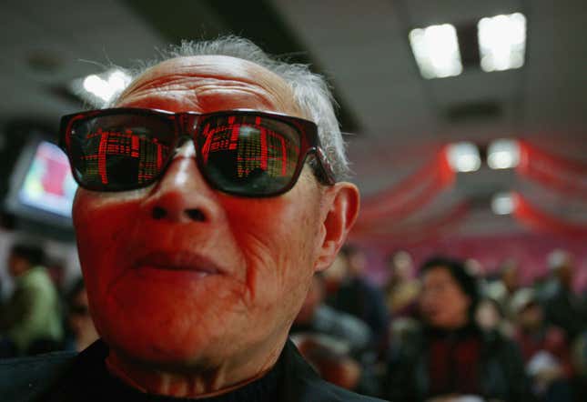 A man with sunglasses on looks at a screen full of stock numbers in awe.