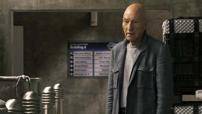 Patrick Stewart as Jean-Luc Picard, standing in an empty corridor. He is surrounded by metallic crates.