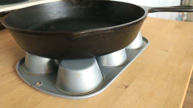 A cast iron skillet sits on an upside down muffin tin.