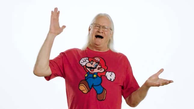 Voice actor and newly minted "Mario Ambassador" Charles Martinet poses with his arms slightly stretched out in a red Mario shirt against a white background for a Nintendo video.