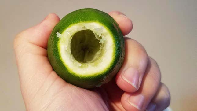 hand holding up the juiced lime, with a hole in one end through which the hollowed-out interior is visible