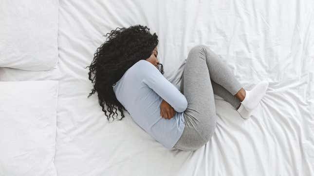 Woman curled up on bed, in pain from stomach cramps