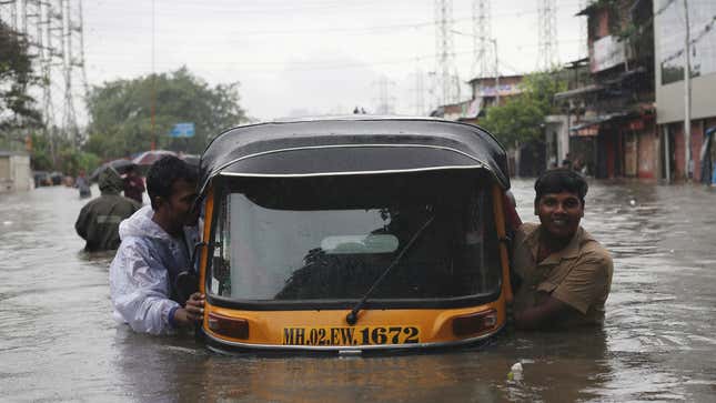 Men push an auto-rickshaw through a flooded road in Mumbai on Sept. 04.