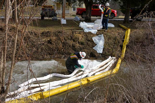 workers in respirators putting plastic booms into stream