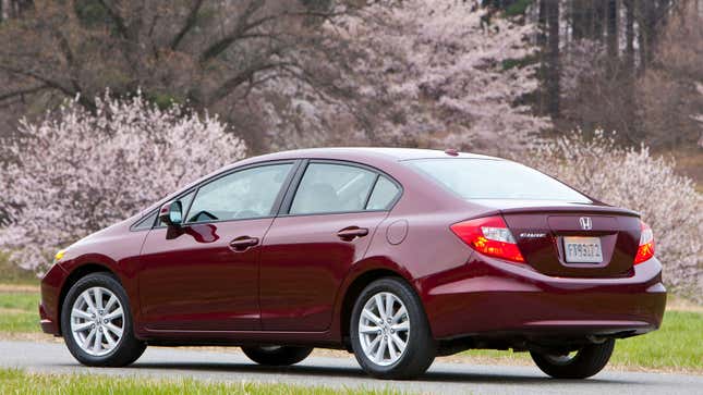 A photo of a burgundy Honda Civic sedan parked near blossom trees. 
