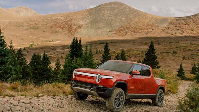 A photo of a red Rivian R1T pickup driving up a gravel path. 
