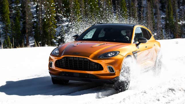A photo of an orange Aston Martin SUV driving in snow. 