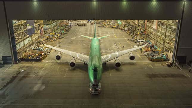 A bare metal green 747 rolls through the mass doors of the production facility