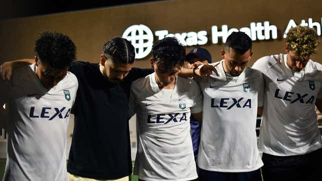 Members of the Dallas United team bow their heads before a game, with owner Edwin Castro amongst them. 