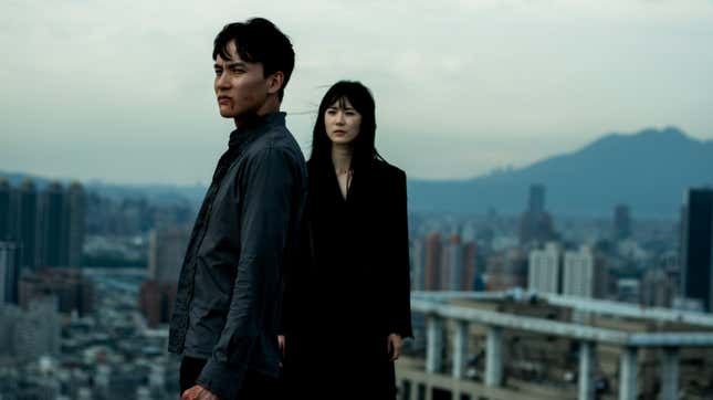 A man with blood on his mouth and a woman dressed in black stand high above a cityscape in the background in a still from Dead & Beautiful.