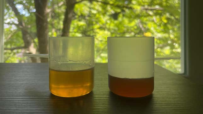 Two cups of liquid, the one on the left (whiskey) being significantly more full than the one on the right (syrup). 