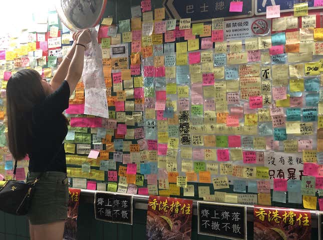 Crystal, a volunteer, puts up a notice directing people to continue putting up sticky notes elsewhere in the underpass due to a lack of space.