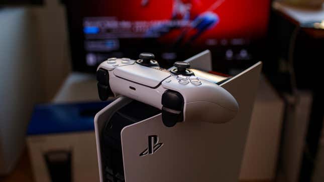 A PlayStation 5 Console with the controller sitting on top of the machine standing in front of a TV showing the splash screen for Marve's Spiderman.