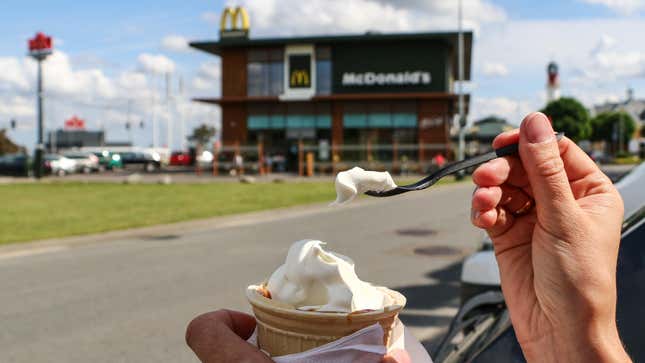 A person with a vanilla soft serve cone in front of a McDonald's