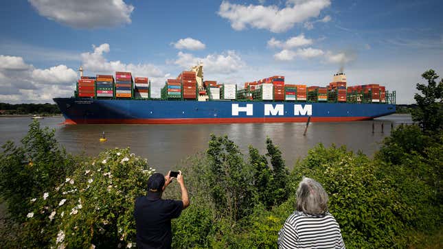 A photo of two people taking a photo of an HMM container ship. 