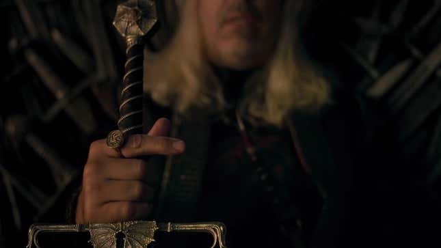King Viserys gripping the hilt of his sword as he sits on the Iron Throne.