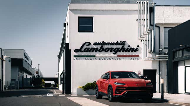 A photo of a red Lamborghini Urus SUV parked outside a building with the company logo on it. 