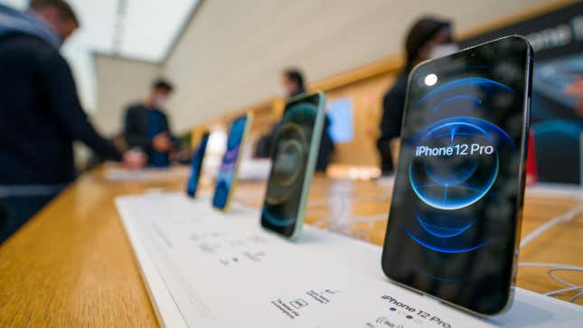 The iPhone 12 and iPhone 12 Pro on display during launch day, all in a row with people perusing the phones in the background.