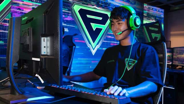 A student sits at a computer and plays a video game. There is a big "E" logo on the wall.