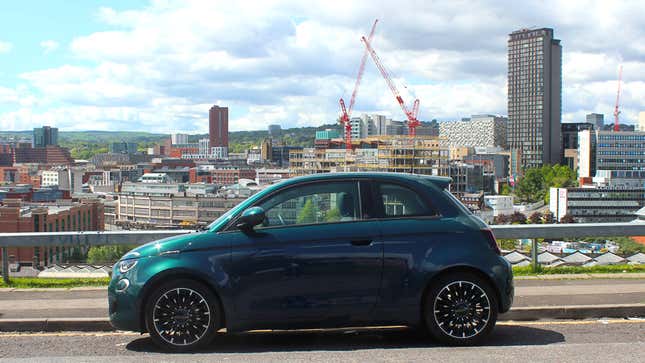 A photo of a Fiat 500 EV in front of a city. 