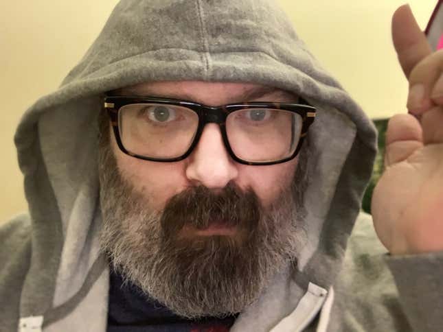 Mike Fahey of Kotaku looks at the camera while wearing a grey hoodie and black rimmed glasses.