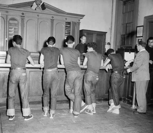 Five boys, all wearing blue jeans and the same dark shirt, stand in front of booking officer at the west 47th street police station in New York, July 31, 1954. The youths were among some 90 persons picked up by police in a drive on juvenile delinquents and "generally undesirable characters." All were round up in Time Square area. (AP Photo/Chris Daly)