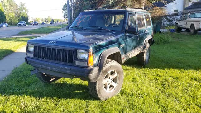 Jeep cherokee four door green sitting on lawn next to sidewalk with $500 written on windshield  and other windows. clearcoat is peeling.