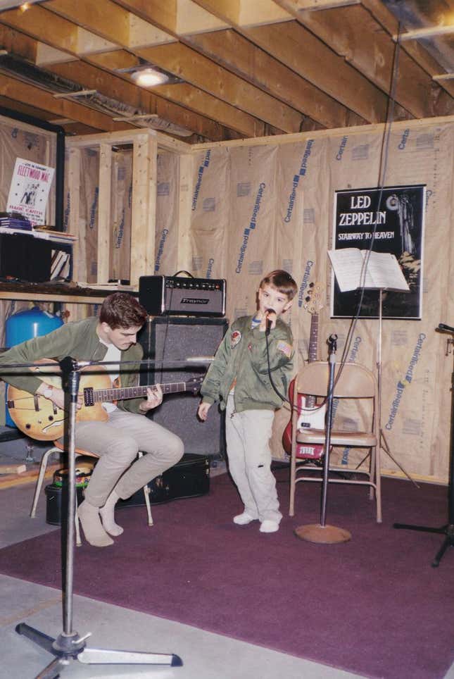 Adult Nickerson plays the guitar while young Nickerson sings with a microphone.