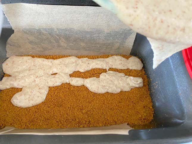 Pouring the second half of the batter over the center layer of cookie crumbs in a loaf pan.