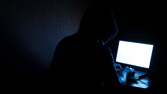A person wearing a hoodie in a dark room types at a computer.