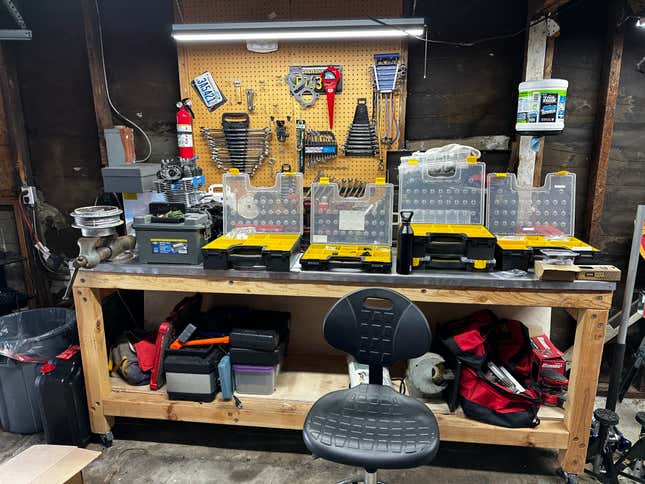 A garage workbench with lots of plastic organizers on it.