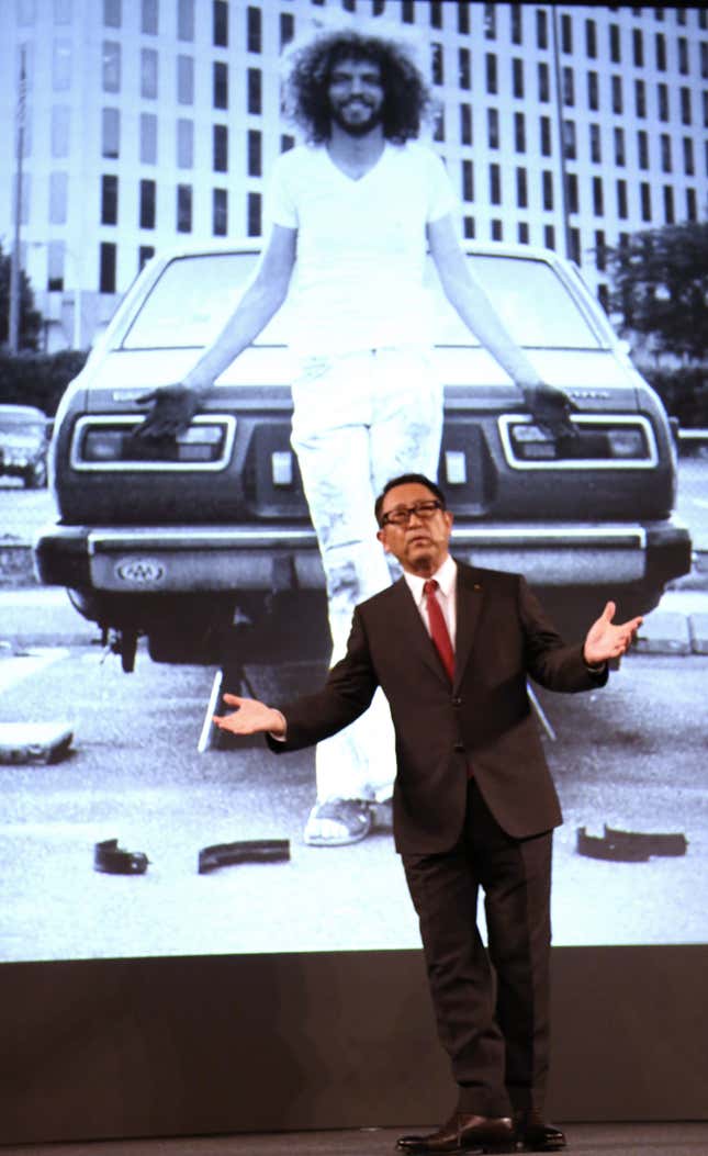 Toyota President Akio Toyoda showing off an old photo of a younger Pratt, working on a Toyota car.