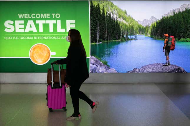 A person pushes a pink suitcase in front of a lit sign for Seattle International Airport