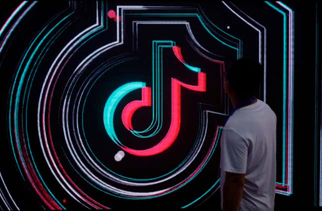 The TikTok logo lit up in neon with a person standing in front of it.