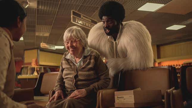 A man in a white feathery jacket looms over a smiling older woman