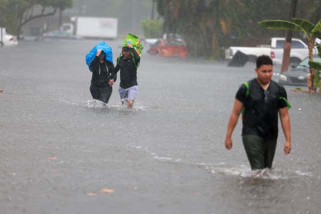 Denis Mendez, Isain Lopez, and Santiago Rojas walk through a flooded street on April 13, 2023 in Fort Lauderdale, Florida. 