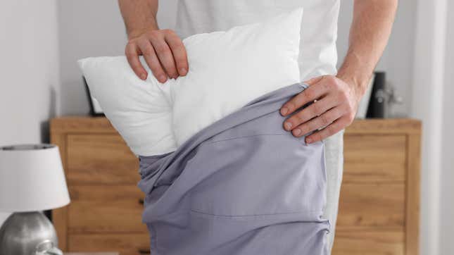 A man stuffs a pillow into a blue pillowcase