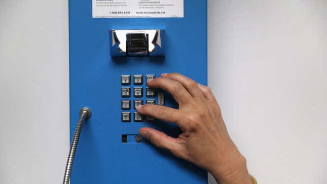A hand presses the keys of a blue prison phone. 