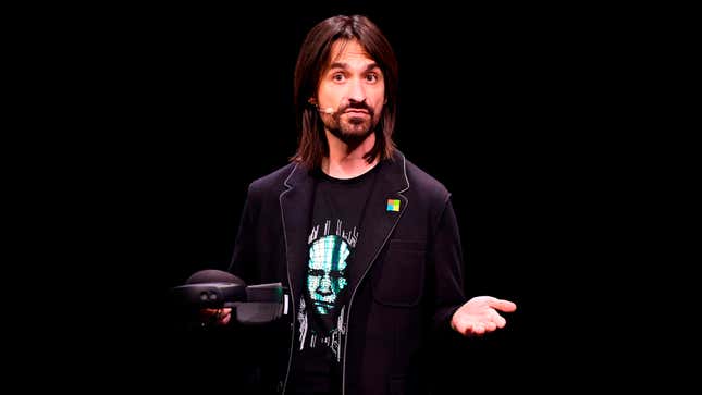 A man with long hair and a beard is standing against a black background while holding a pair of HoloLens glasses.