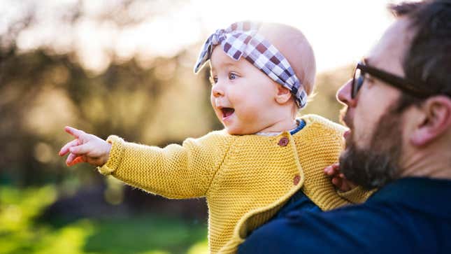 baby girl smiling and pointing off in distance while father holds her