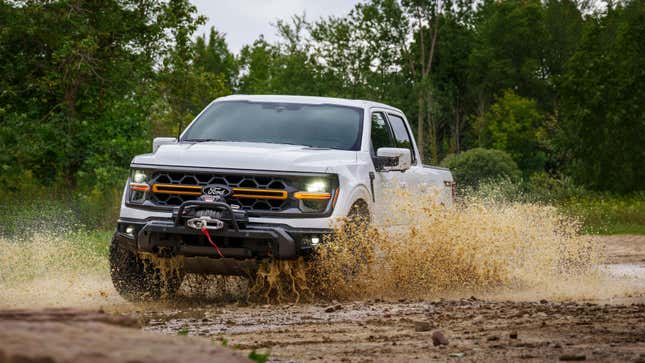 A white Ford F-150 Tremor driving through mud 
