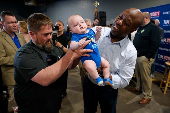 Republican presidential candidate South Carolina Sen. Tim Scott holds 3-month old Sawyer Thompson, of Council Bluffs, Iowa, as his father Jeff, left, looks on during a town hall meeting on May 24, 2023, in Sioux City, Iowa.