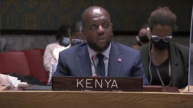 A man behind a sign that says "KENYA".
