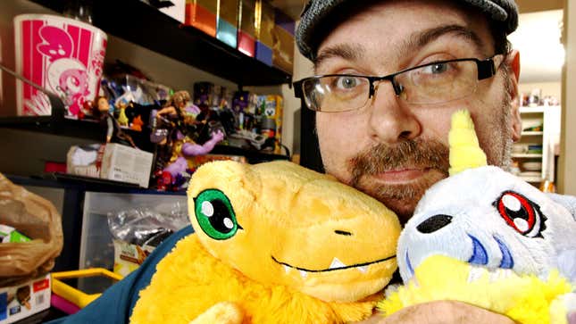 Mike Fahey of Kotaku holds two Digimon plushies close to his face while he smiles.