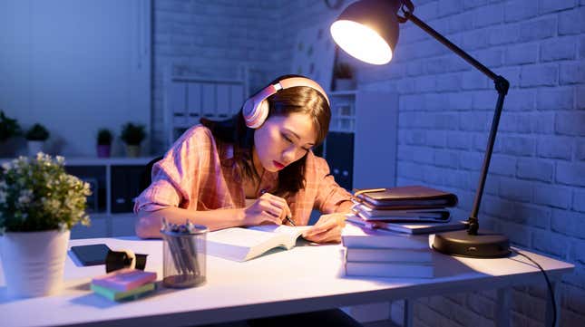 woman studying at night in the dark with a lamp on and headphones on