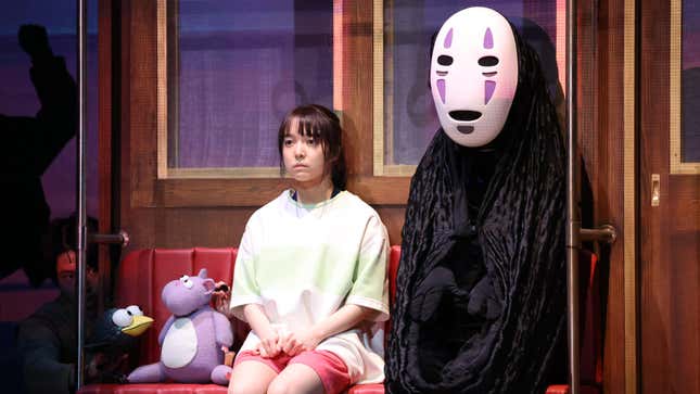 In a scene from the Spirited Away stage play, Chihiro and No Face sit on a train with Boh mouse.