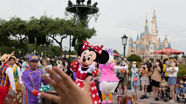 Minnie Mouse points at a camera in front of a crowd of people taking pictures in front of the giant castle structure at Dinsey Shanghai.