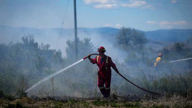 A firefighter directs water on a grass fire burning on an acreage behind a residential property in Kamloops, British Columbia, Canada, on June 5, 2023.